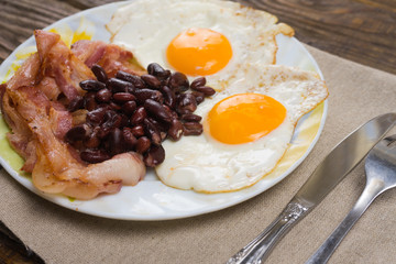 Plate with scrambled eggs, bacon and beans on a wooden rustic table.