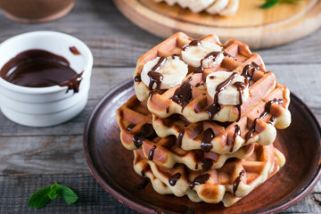 Belgian waffles with chocolate syrup and banana slice on a plate on a wooden background
