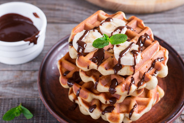 Belgian waffles with chocolate syrup and banana slice on a plate on a wooden background