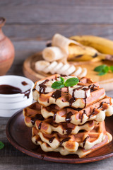 Belgian waffles with chocolate syrup and banana slice on a plate on a wooden background