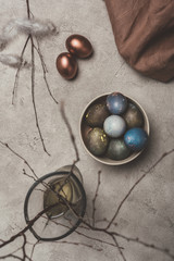 top view of painted easter eggs in bowl and willow branches in vase on concrete surface