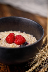 Still life of a healthy breakfast. Oatmeal with blueberries and fresh raspberries on a wooden background with dry ears.