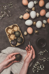 cropped view of man painting easter eggs and putting them into tray, flowers, quail and chicken eggs near