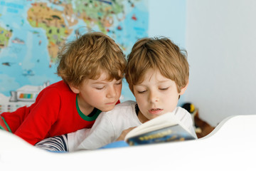 Two little kids boys in pajamas reading a book in bed.
