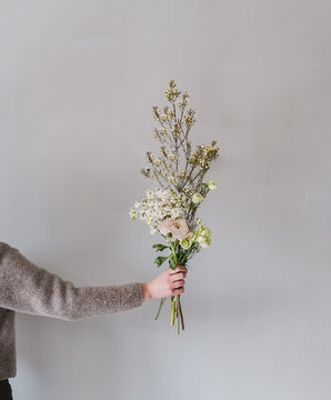 Woman's hand holding bouquet of flowers against gray wall