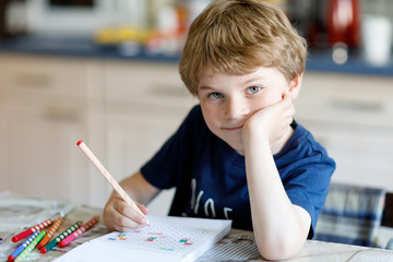 Happy smiling kid boy at home making homework writing letters with colorful pens