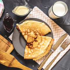 Top view of the Russian dish pancakes, milk, jam, white chocolate, towel, potholder, knife and fork.