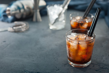 Alcohol cocktail with cola and ice with two cocktail tubes on a gray background in the background bar stock