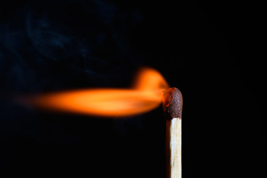 Match with strongly flaring flame beveled on its side on a black background closeup