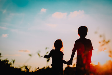 little boy and girl silhouettes holding hands at sunset