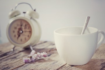 A white coffee cup with Alarm clock on the wood on white background, Vintage filter style, Vintage concept