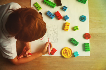 child solving labyrinth, building from plastic blocks