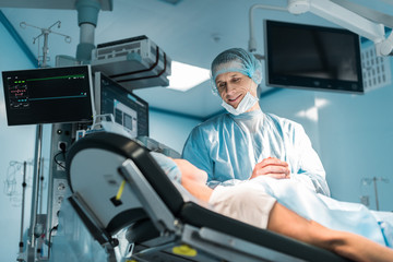 bottom view of smiling doctor and patient holding hands in operating room