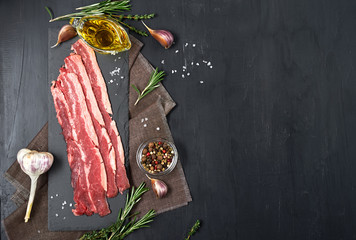 Bacon rashers with rosemary, garlic and olive oil isolated on black background. Top view.