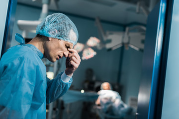 side view of tired doctor touching nose bridge in surgery room