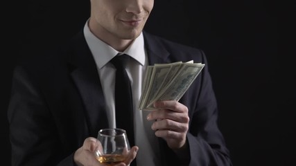 Businessman holding dollar cash and drinking cognac, celebrates income increase - Powered by Adobe
