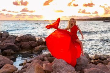 Beautiful young sexy blonde, posing in evening red dress on sea quay on the sunset