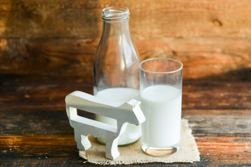 milk bottle, glass of milk, a figure of a cow the concept of a village power, farm-fresh products on a natural wooden background