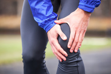 Cropped shot of a young runner holding his injured knee while running.