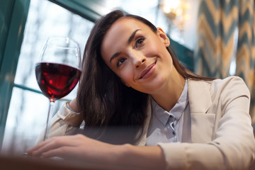 Wine for health. Gay elegant cute woman enjoying glass of wine while sitting near window and looking up