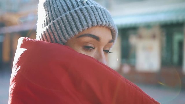 Sun shines over a girl in red winter jacket standing on the street