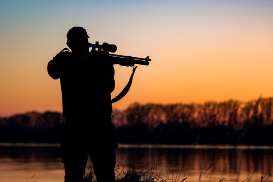 silhouette of hunter with rifle on the background of sunset. man with a gun against the evening sky and the river