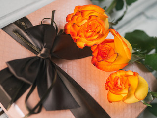 Beautiful gift for the holiday and a bouquet of orange roses on the table