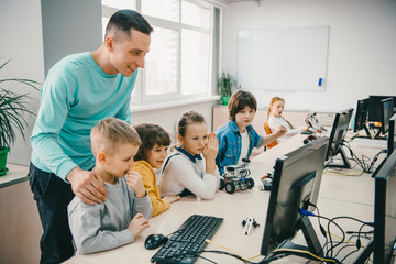 happy young teacher helping his teen students with diy robot on stem education class
