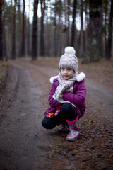 Little cute girl posing on the road in the pine forest in autumn time