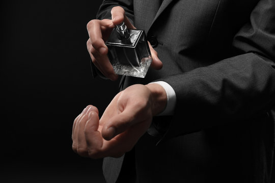 Handsome man in formal suit and with bottle of perfume on dark background, closeup