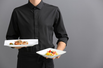 Waiter holding plates with dishes on gray background