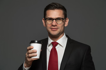 Successful businessman with glasses and formal suit posing with coffee mug on gray background