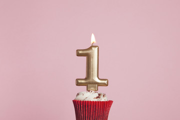 Number 1 gold candle in a cupcake against a pastel pink background