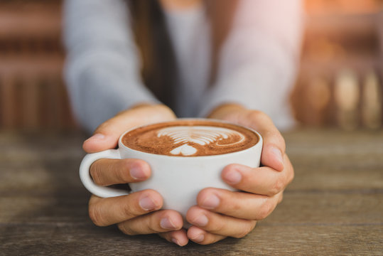 Woman hands holding cup of hot coffee latte cappuccino with heart shaped. Love, Wedding and Valentines day concept.