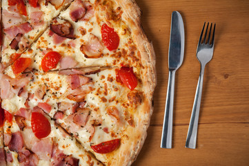 Top view of tasty Italian pizza, fork and knife on wooden table.