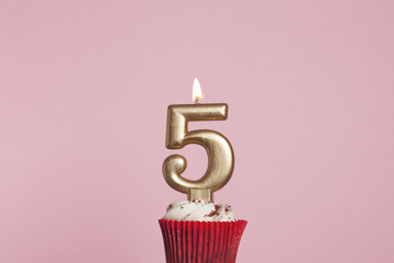 Number 5 gold candle in a cupcake against a pastel pink background