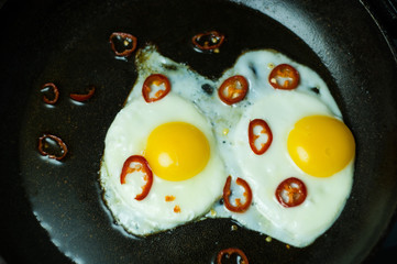 Two fried eggs with chili pepper in a skillet.
