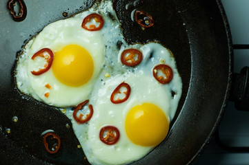 Two fried eggs with chili pepper in a skillet.