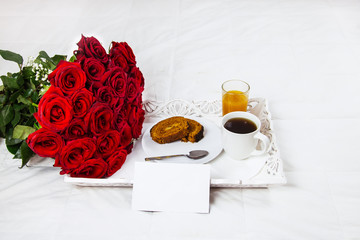 Breakfast in bed, celebrate valentines day, womens day or birthday. White bed, large bouquet of red roses. In the background of a pillow, a bedside table unfocus. copy space, free space.