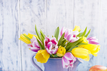 A bouquet of colored tulips in a vase on a wooden white background. A gift in the spring. Free space for text or a postcard.