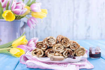Homemade traditional pancakes with jam for spring carnival. Russian breakfast. Bright flowers of tulips. Blue background. Free space for text or a postcard.