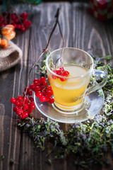 Herbal tea from the viburnum decoction of red sea buckthorn berries and thyme in a transparent glass mug in the village on a wooden table