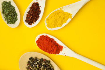 Wooden and plastic spoons with dry spices and fresh herbs on a yellow background with copy space, top view, close up