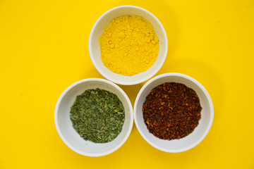 Plastic cups with dry spices and fresh herbs on a yellow background with copy space, top view, close up