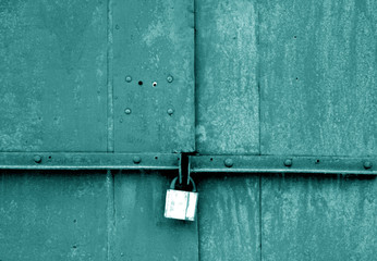 Old padlock on metal gate in cyan tone.
