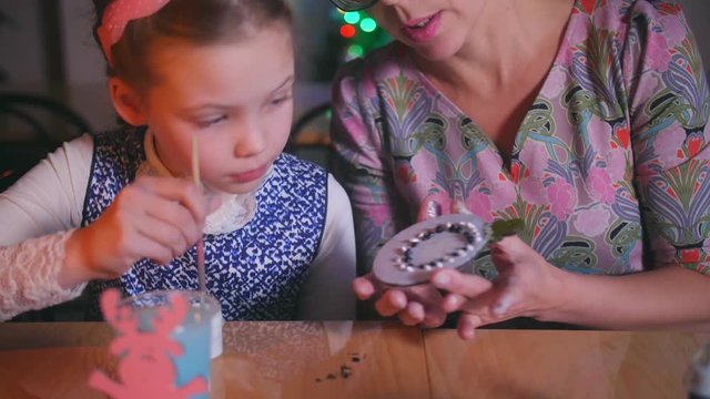 mother teaches her daughter to make a Christmas toy.