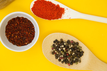 Plastic cups and spoons with dry spices and fresh herbs on a wooden cutting board with yellow background, top view, close up