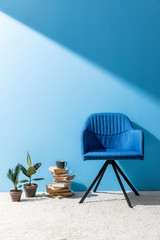 armchair with books and ficus pots in front of blue wall