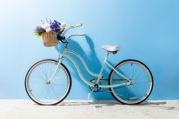 side view of bicycle with flowers in basket in front of blue wall
