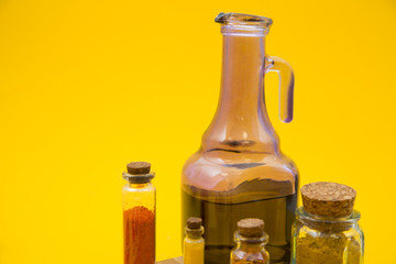 Glass bottles and jug with dry spices and fresh herbs on a wooden cutting board with yellow background, top view, close up